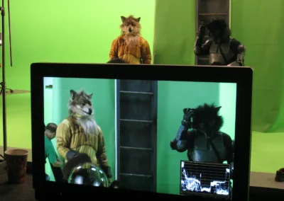 Two actors on a greenscreen in wolf humanoid costumes, while also on view in a video monitor.