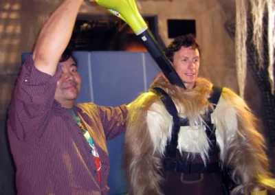 A man aiming a leaf blower inside another man's costume in order to help cool him off.