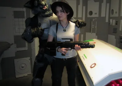 An actor in a wolf humanoid costume posing with a woman holding a prop gun, on a spaceship set.