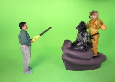 Behind the scene picture of two actors costumed as wolf humanoid characters who are supposed to be riding on the hovercraft. A production assistant is pointing a leaf blower at them, to help with the look of motion.