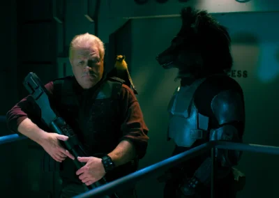 Two actors, one man, and one wolf humanoid, with a bat puppet on the man's shoulder, standing on a spaceship set.